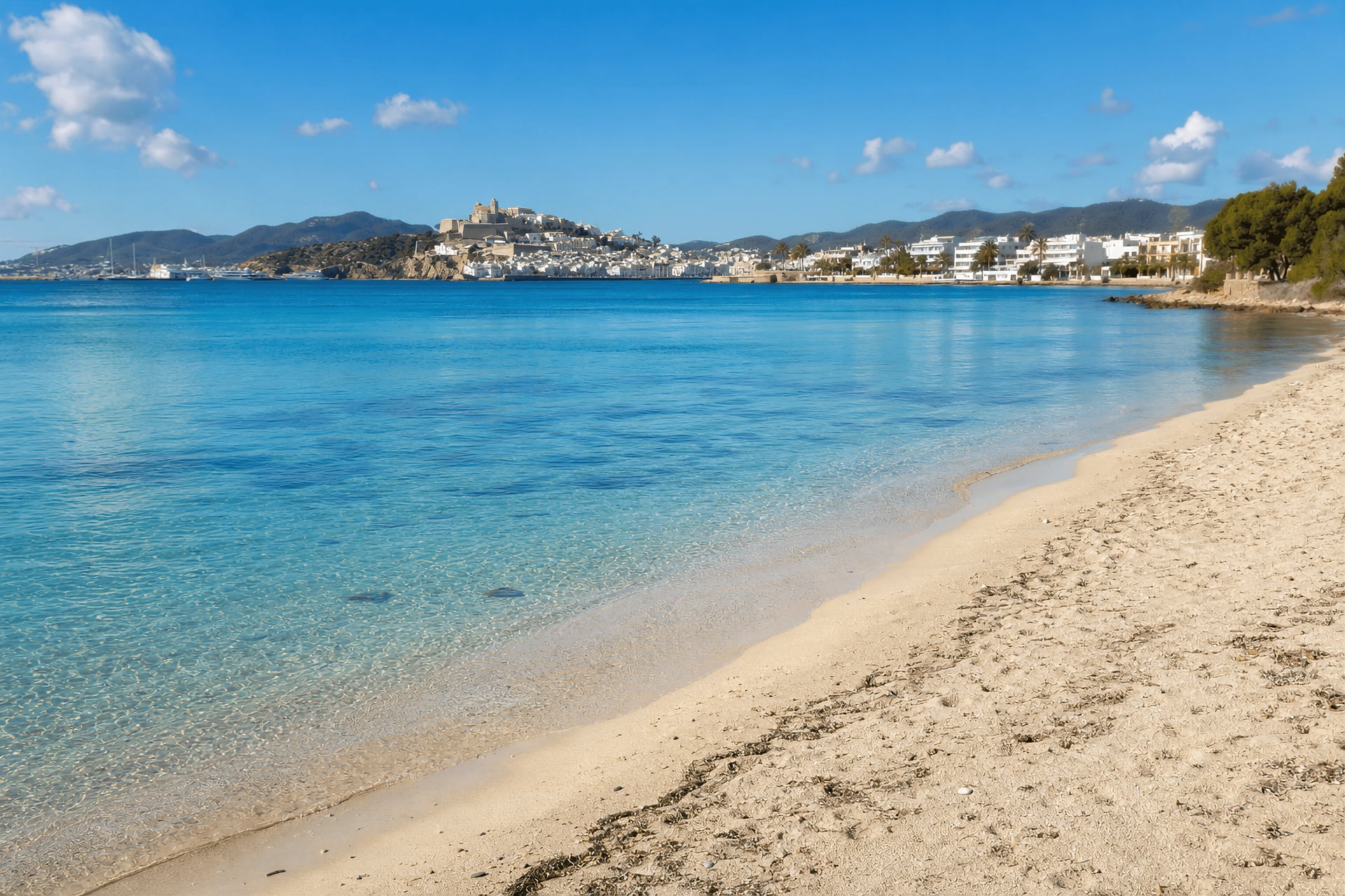 Bright afternoon view of Talamanca beach near Ibiza Town with calm water and the harbour beyond