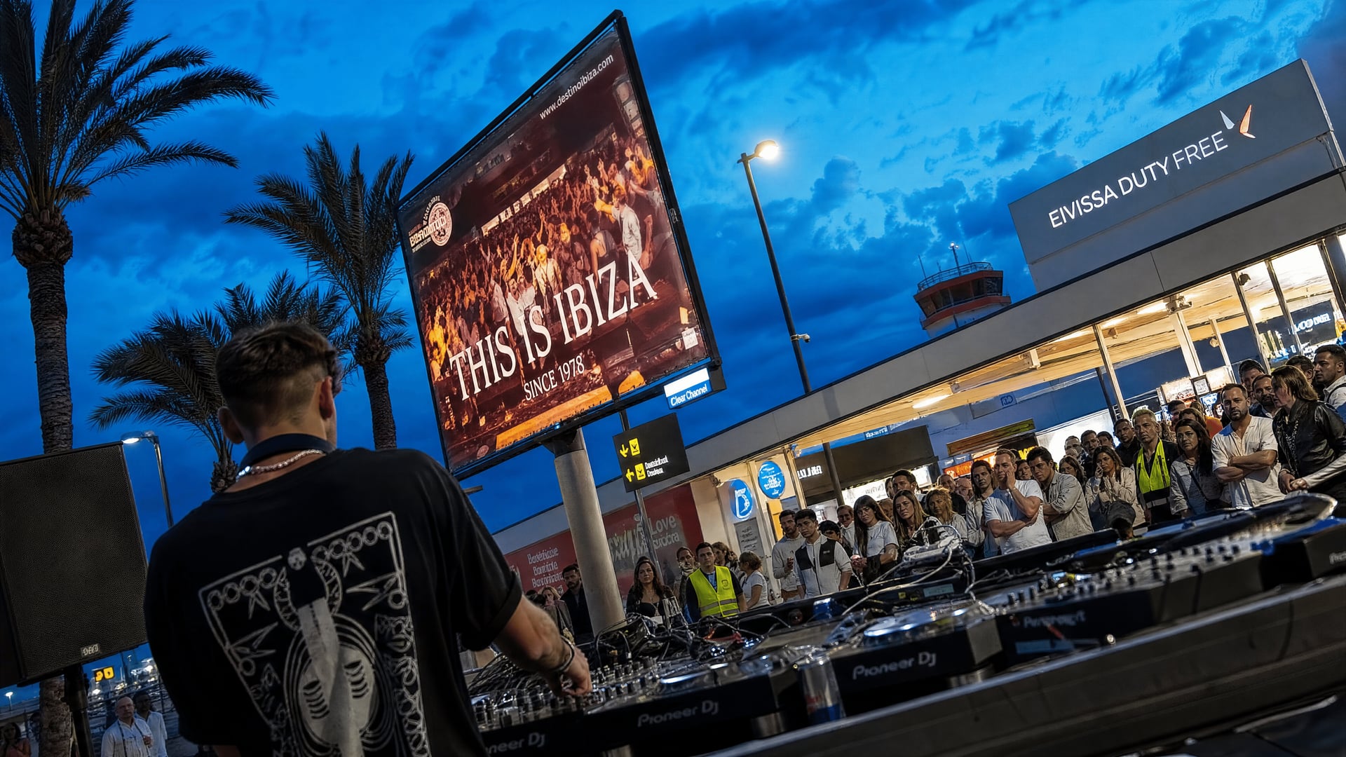 DJ setup beside nightclub advertising in Ibiza Airport’s duty-free arrivals area